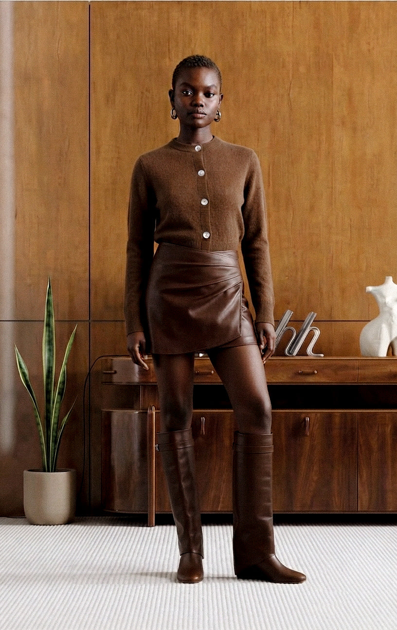 A model stands in a warm, wood-paneled room wearing a coordinated brown outfit consisting of a mock-neck long-sleeve knit top with buttons, a fitted mini skirt, matching leggings, and tall boots.