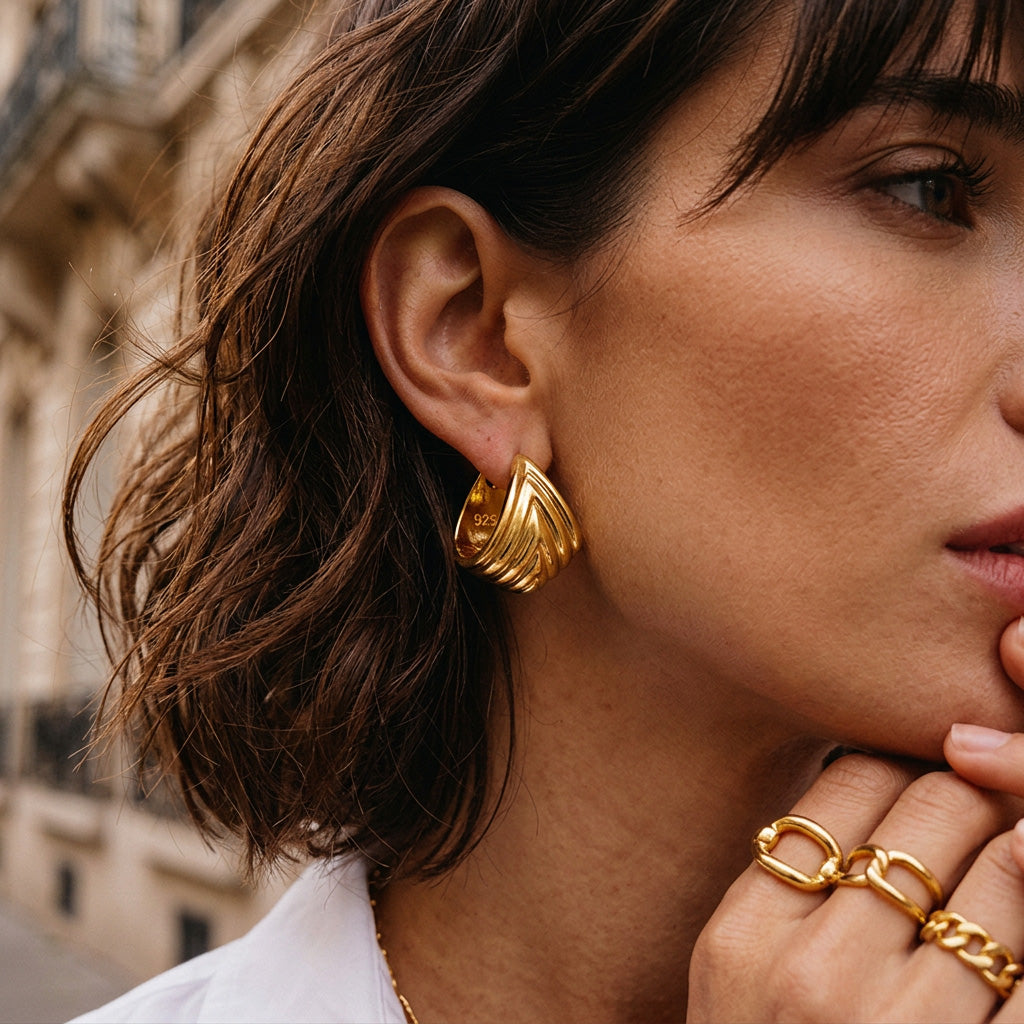 Close-up of a woman wearing gold hoop earrings and a ring, with a blurred background.